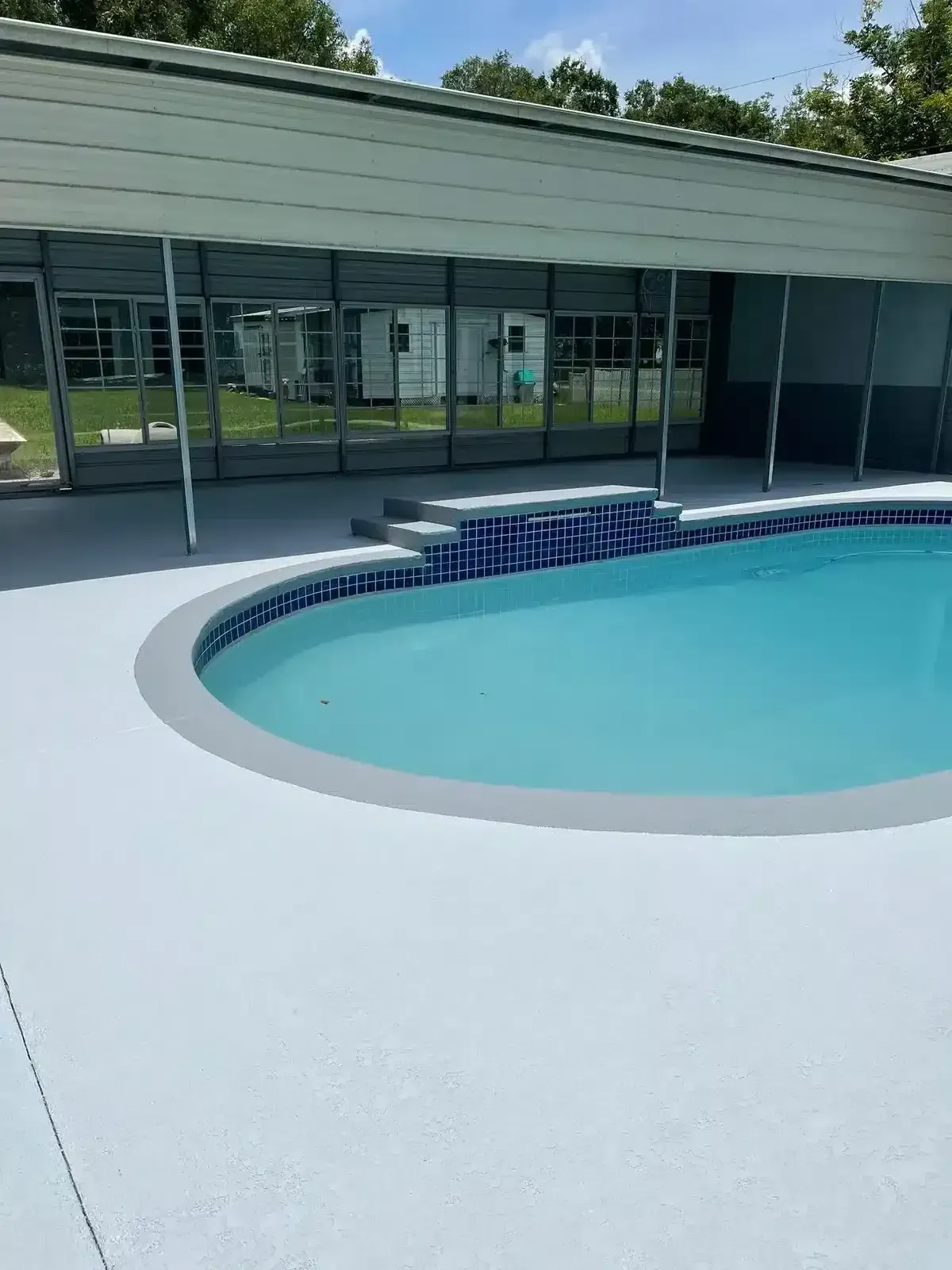Outdoor pool with light blue water and a white deck beside a modern building with glass walls