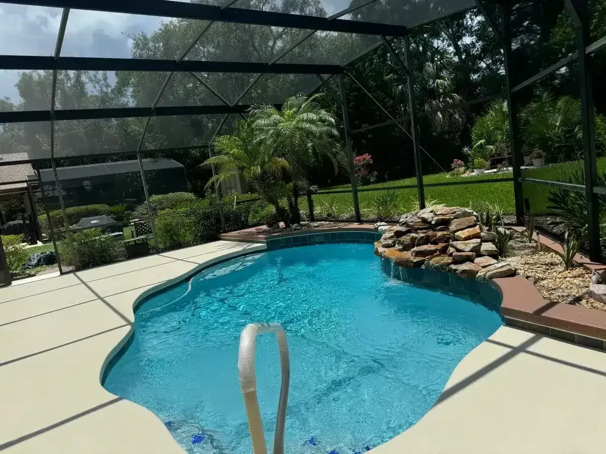 Backyard pool with screened enclosure, blue water, and rock waterfall feature