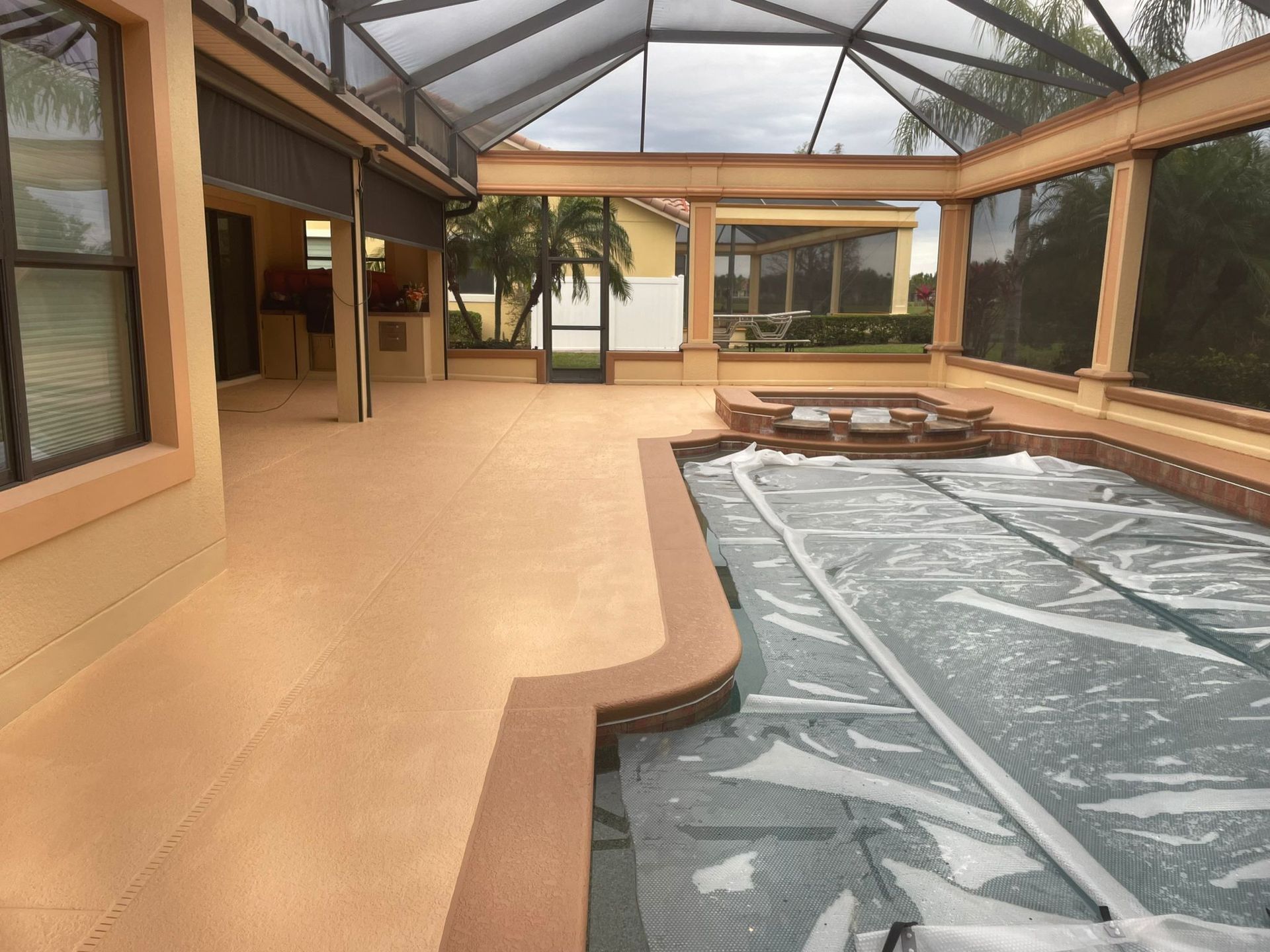 Empty drained swimming pool beside lounge chairs and trees in a sunny courtyard