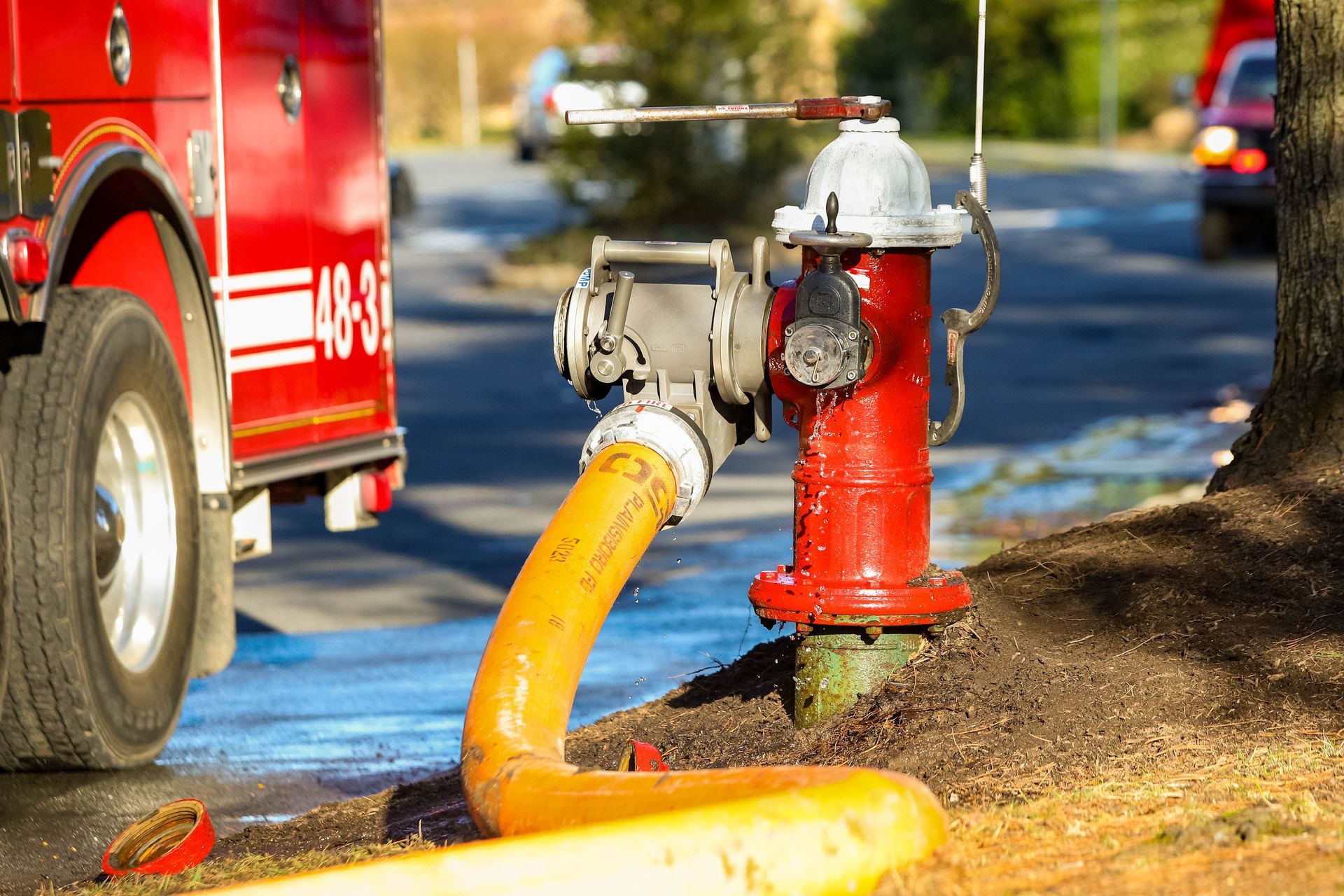 Fire hydrant attached to a large supply hose delivering water to a nearby fire engine.