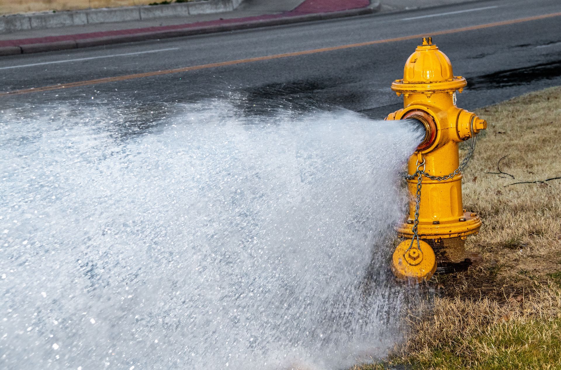 Yellow fire hydrant releasing a strong stream of water onto the grass beside the road. Yellow fire hydrant releasing a strong stream of water onto the grass beside the road.