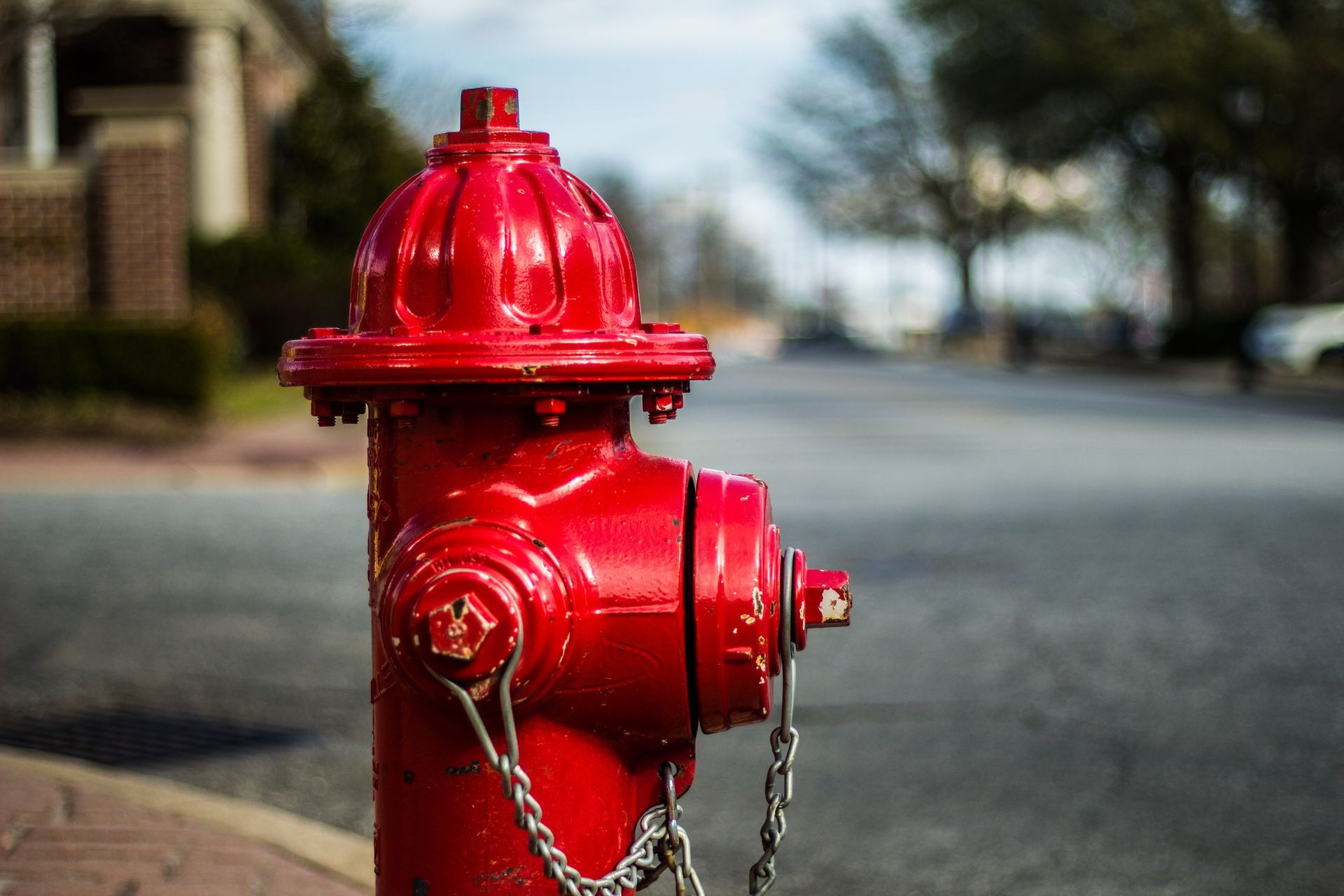 Bright red fire hydrant standing on a street corner with buildings and trees in the background. Bright red fire hydrant standing on a street corner with buildings and trees in the background.