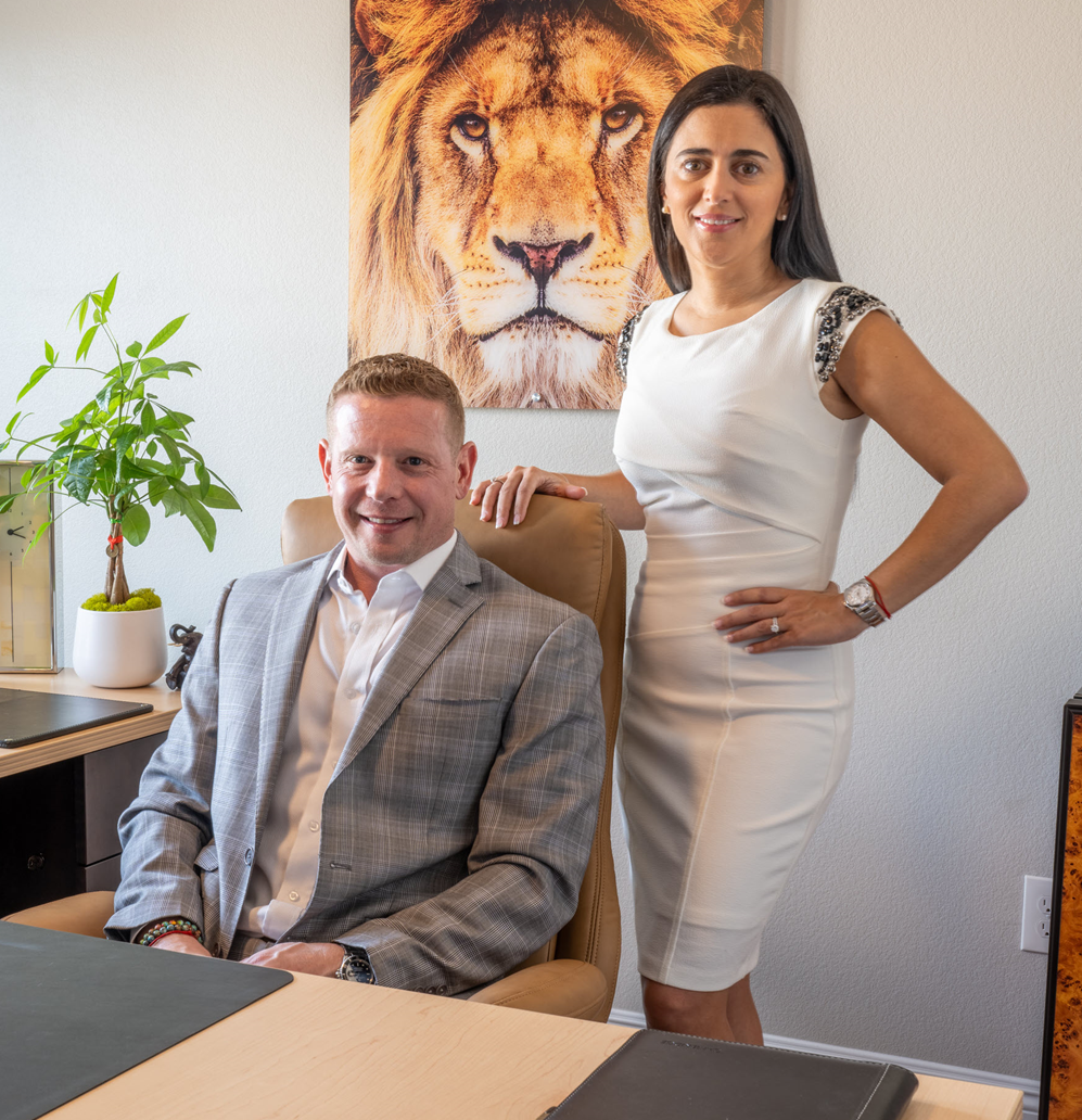 A man and a woman are posing for a picture in front of a lion painting on the wall.
