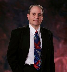 A man in a suit and tie is standing in front of a red background.