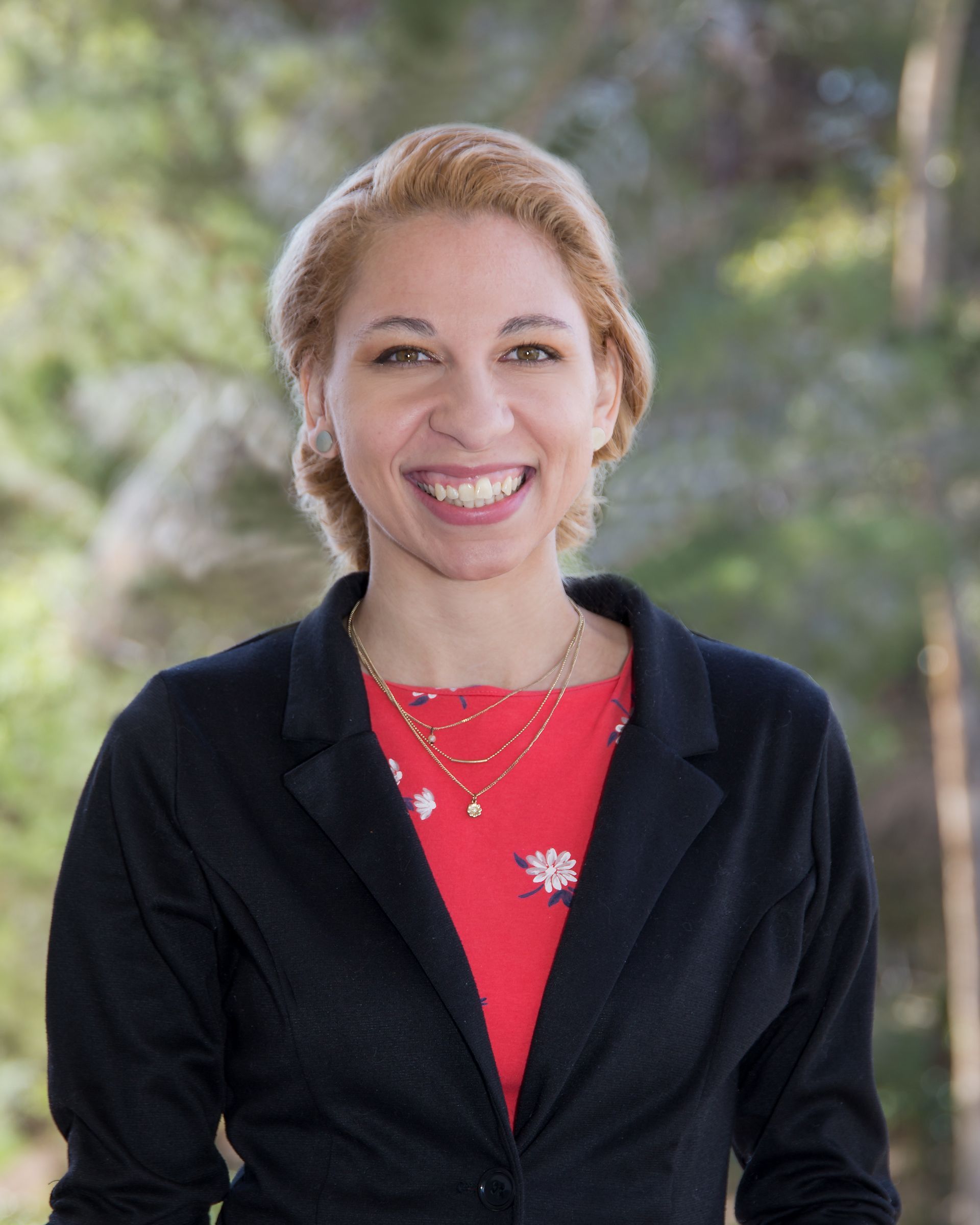 A woman wearing a black jacket and a red shirt is smiling for the camera.