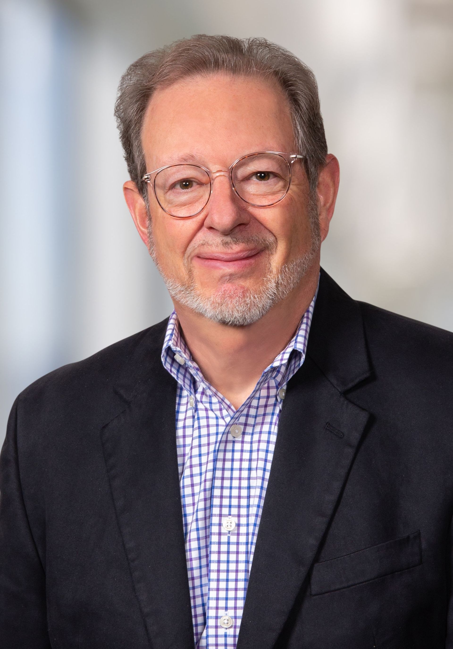 A man wearing glasses and a suit is smiling for the camera.
