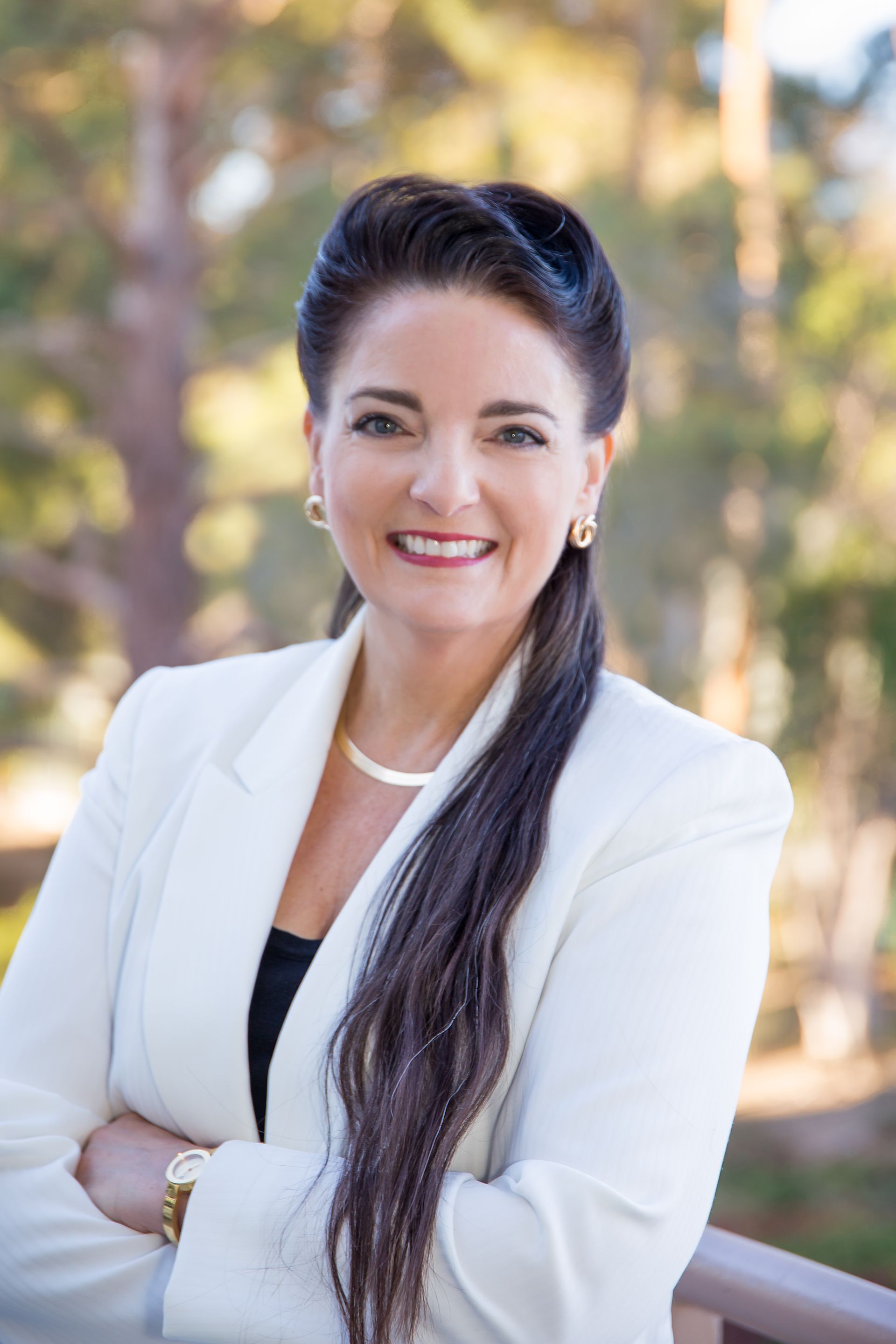A woman in a white jacket and black top is standing with her arms crossed and smiling.