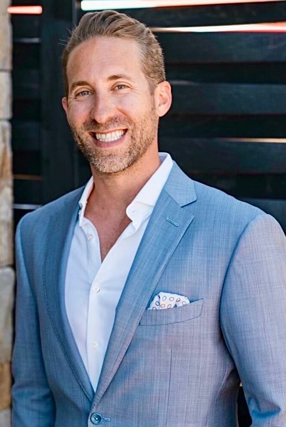 A man in a blue suit and white shirt is smiling for the camera.