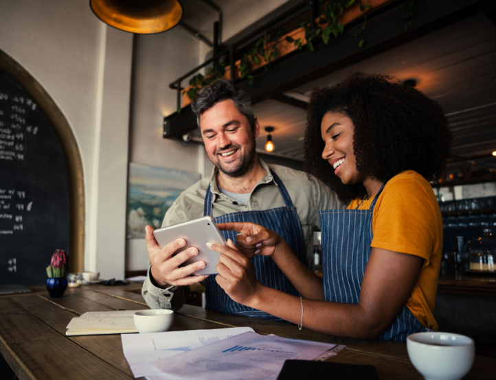 A man and a woman are sitting at a table looking at a tablet.