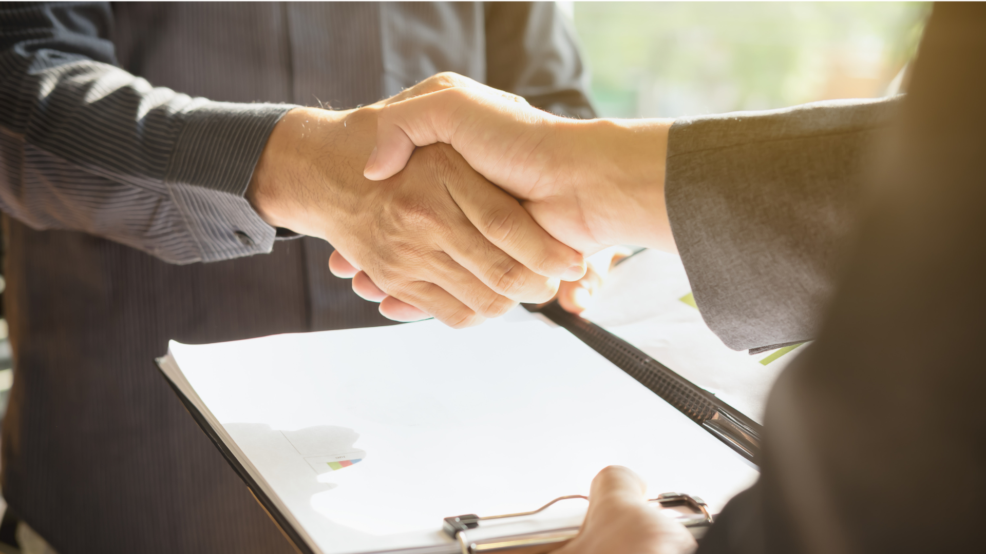 Two men are shaking hands over a clipboard.