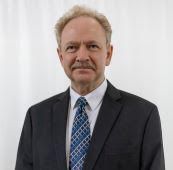 A man in a suit and tie is standing in front of a white wall.