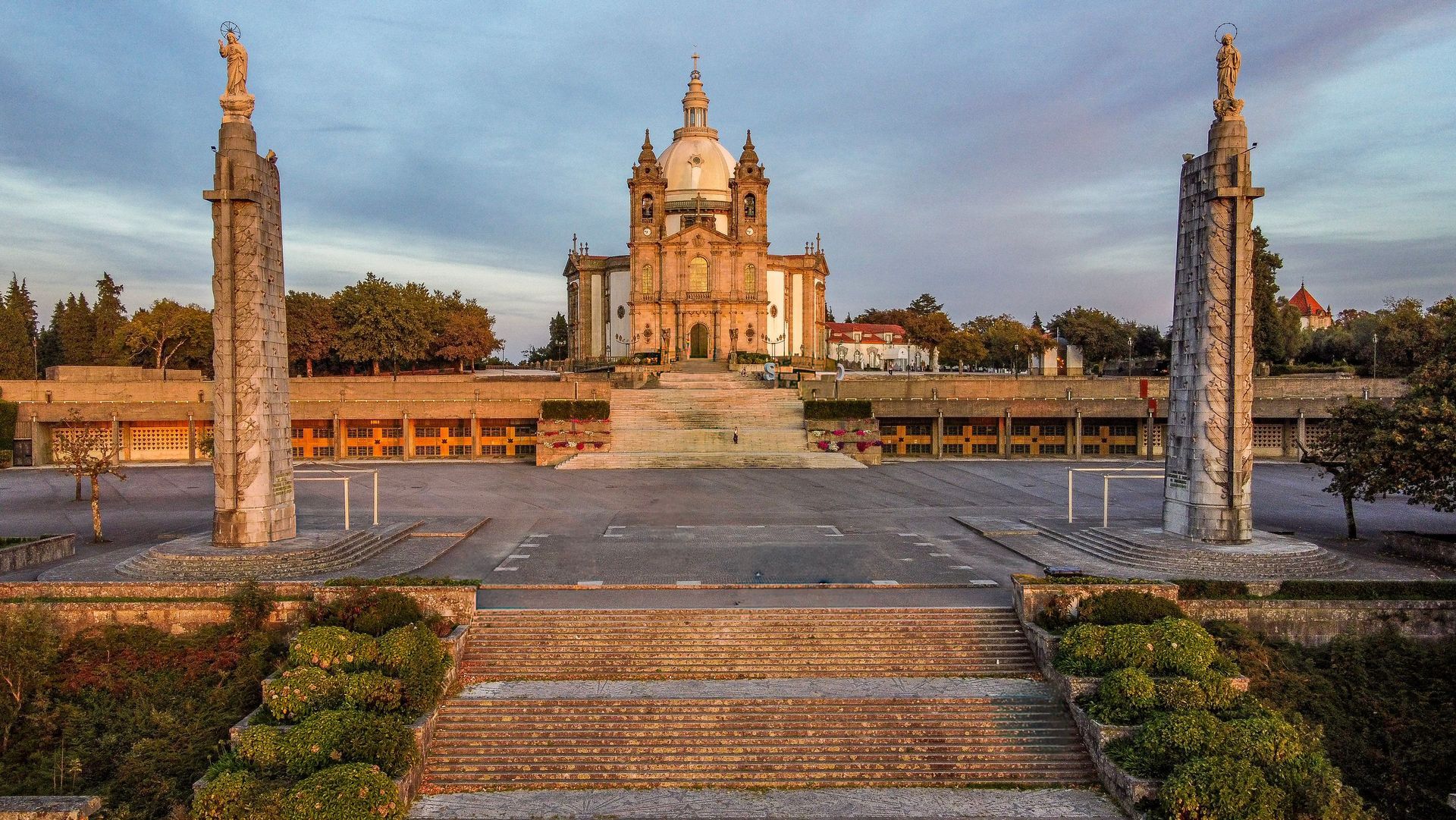 Un grand château historique au coucher du soleil, encadré par des marches en pierre, des fontaines et des allées de jardin.