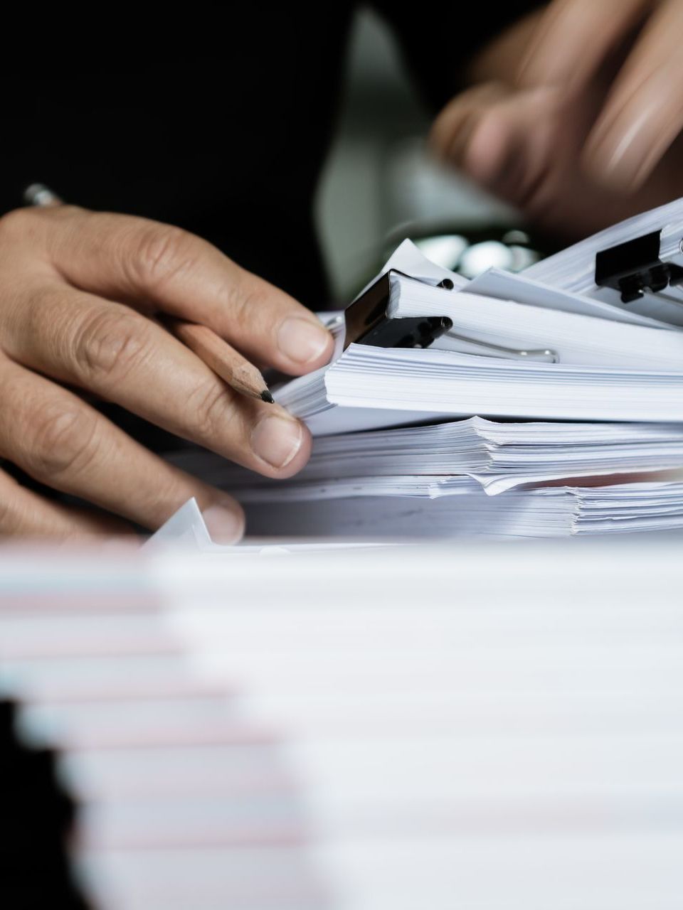 A person is holding a piece of paper over a pile of papers.