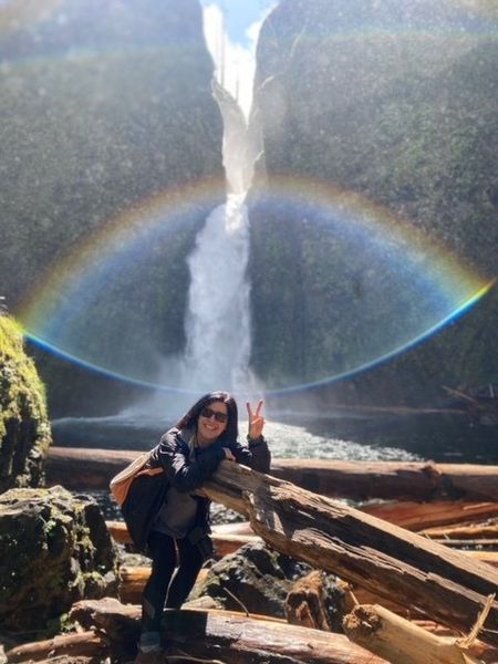 Cannon Beach Haystack Rock sunset Woman poses with peace sign in front of waterfall and rainbow.