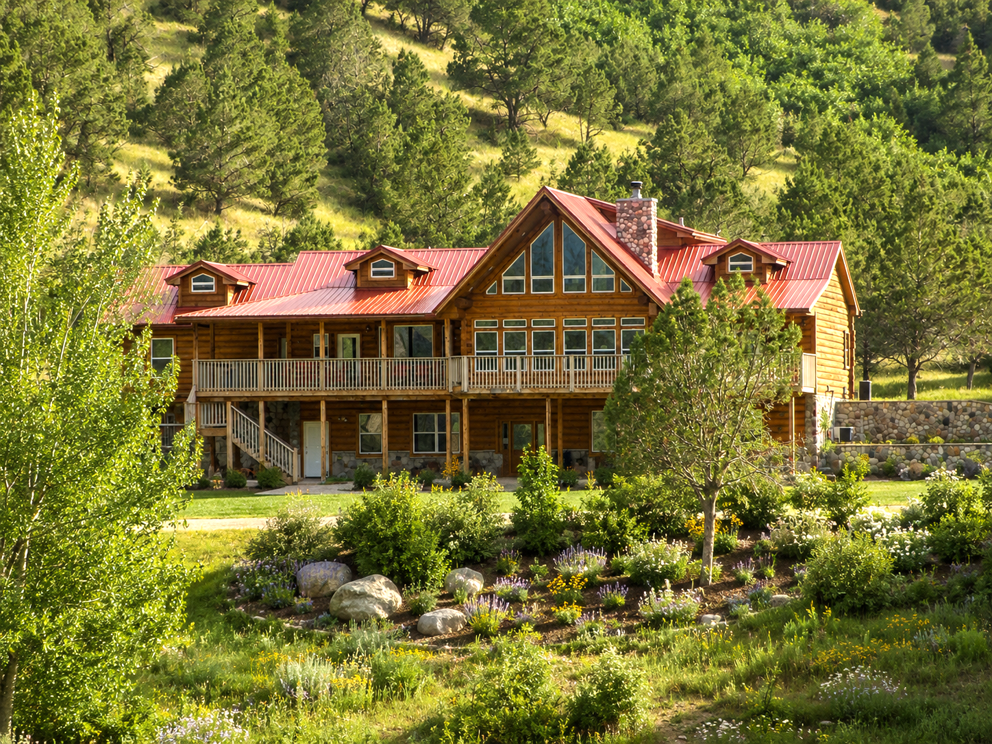 Rustic mountain lodge with red roof amid lush green forest and garden