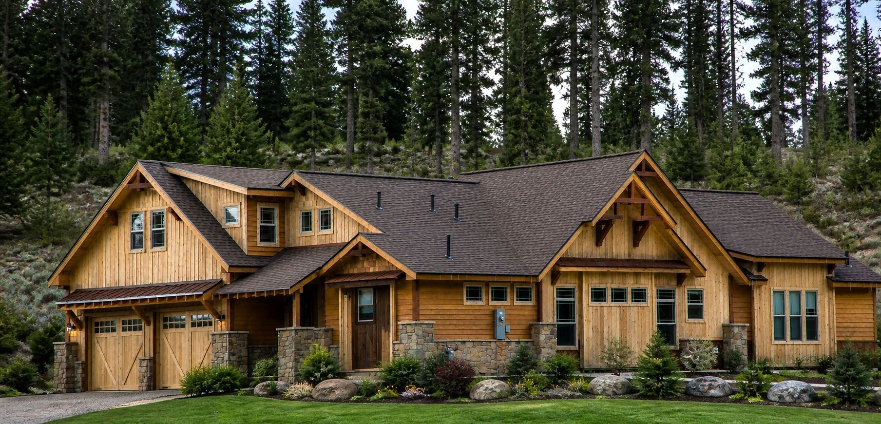 Wooden mountain cabin with tan siding, gabled roof, and tall pine trees in the background