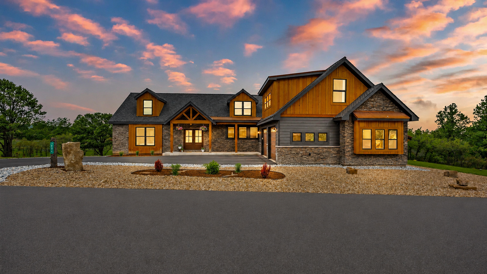 Large rustic house with warm lights at sunset, stone driveway, and cloudy pink sky