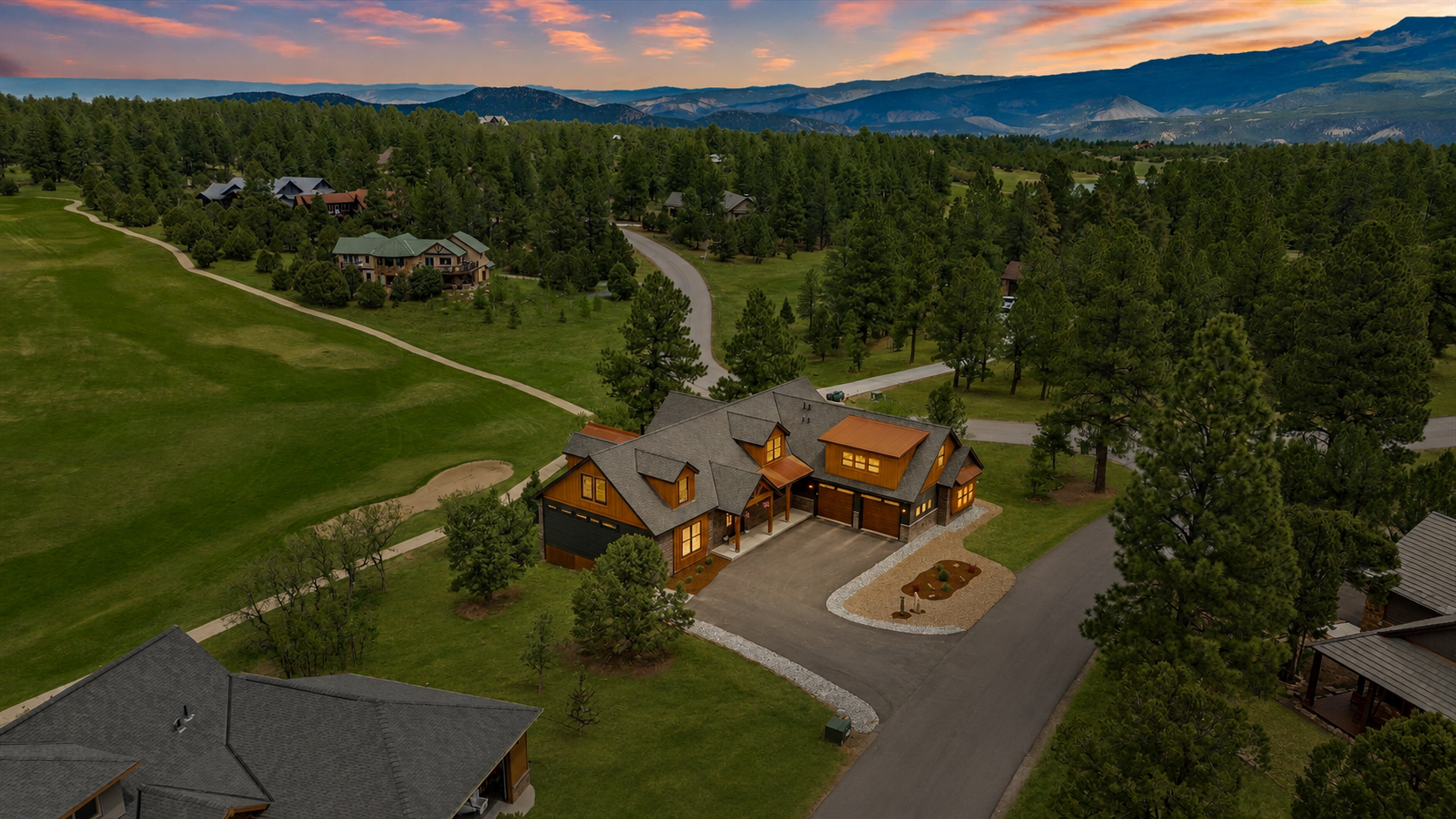 Aerial view of a large house in a wooded mountain setting at sunset