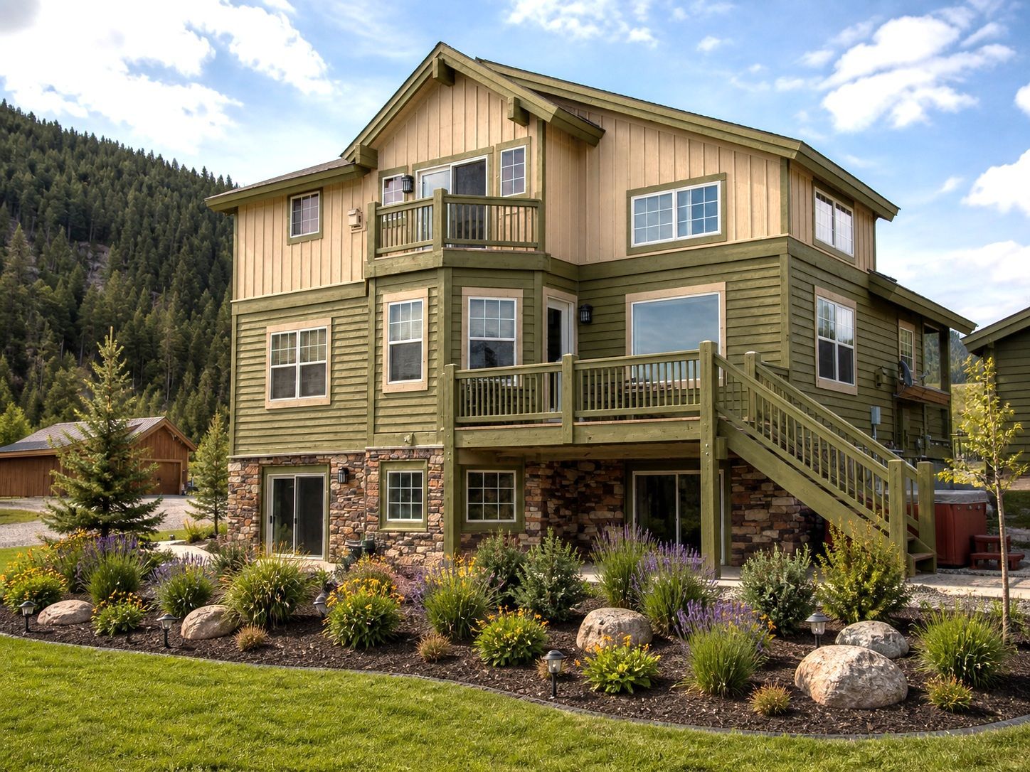 Modern two-story house with beige siding, stone accents, and a landscaped garden in a mountain setting