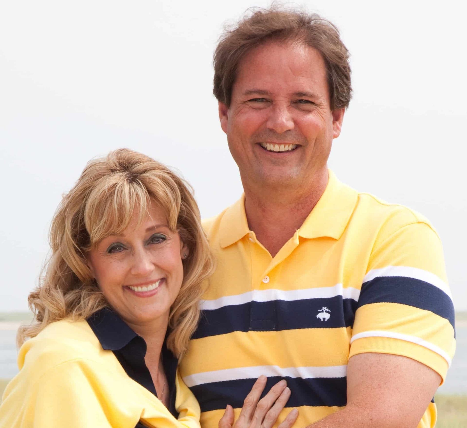 Two smiling people in yellow shirts posing together against a white background