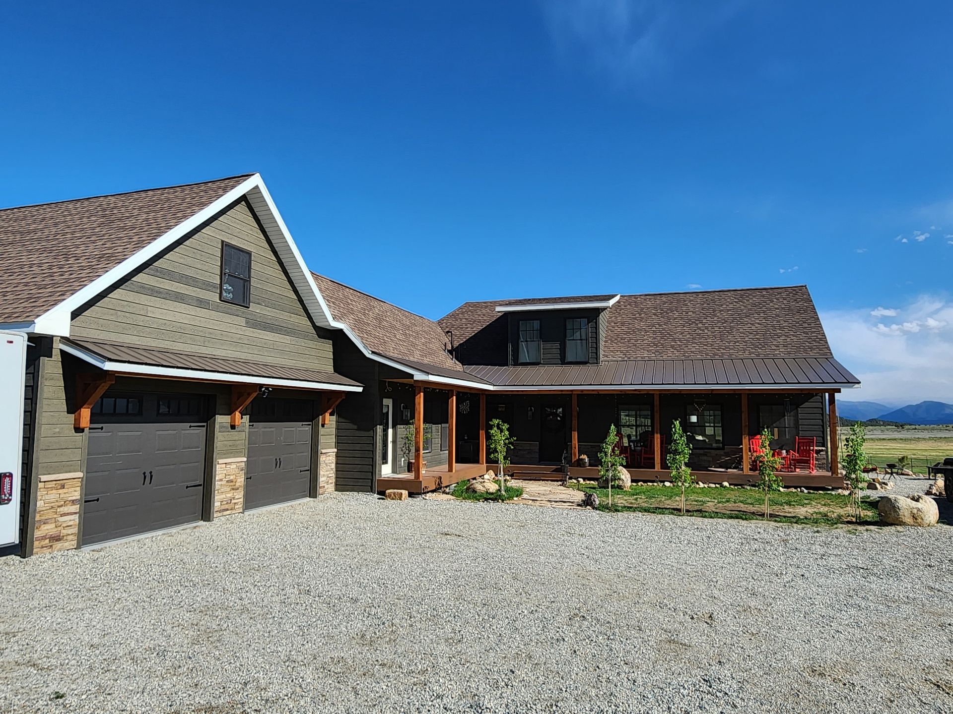 Stone house with brown roof and garage, set on a gravel driveway under a clear blue sky