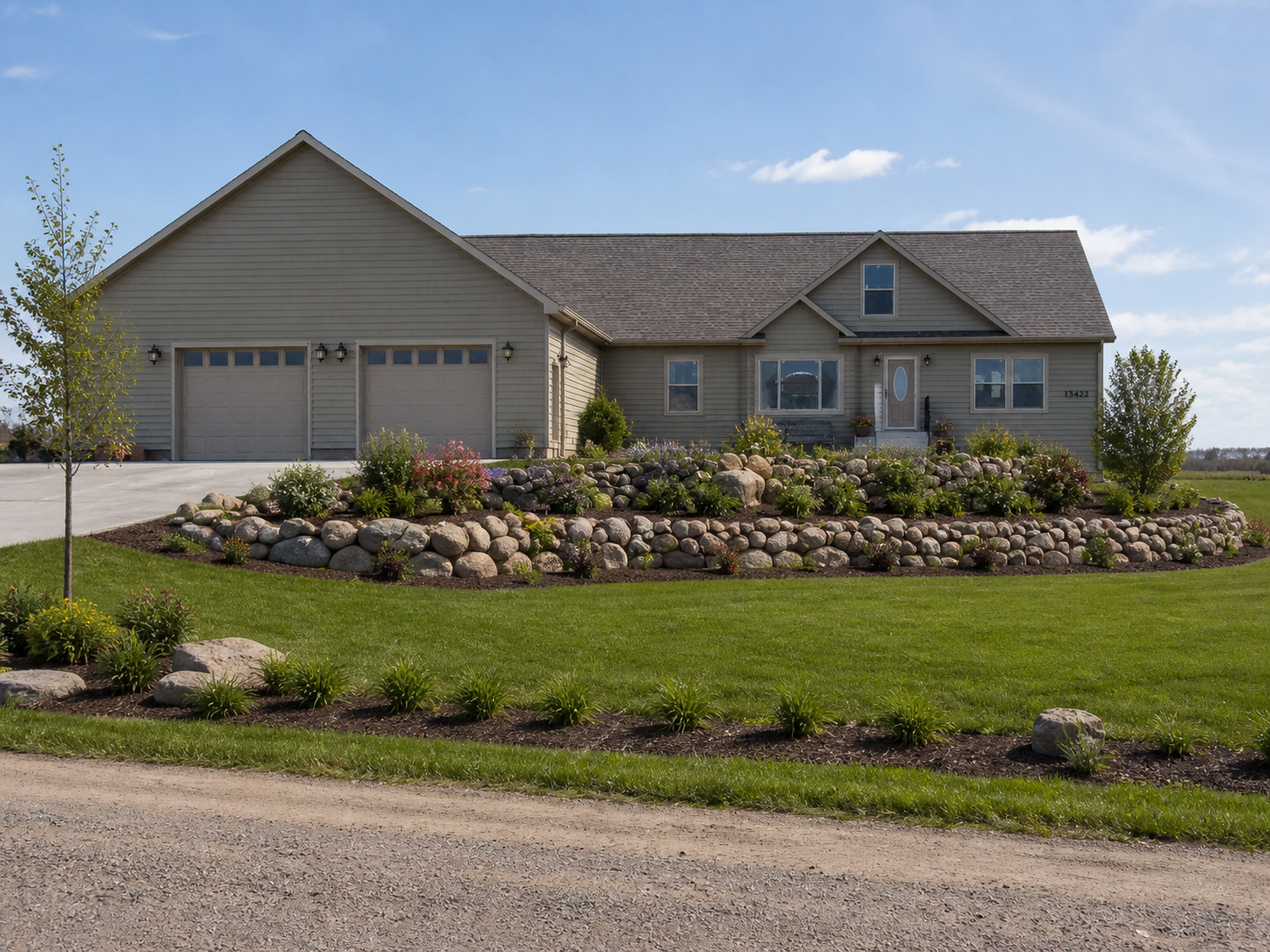 Single-story beige house with attached garage, stone landscaping, and gravel driveway under a clear sky