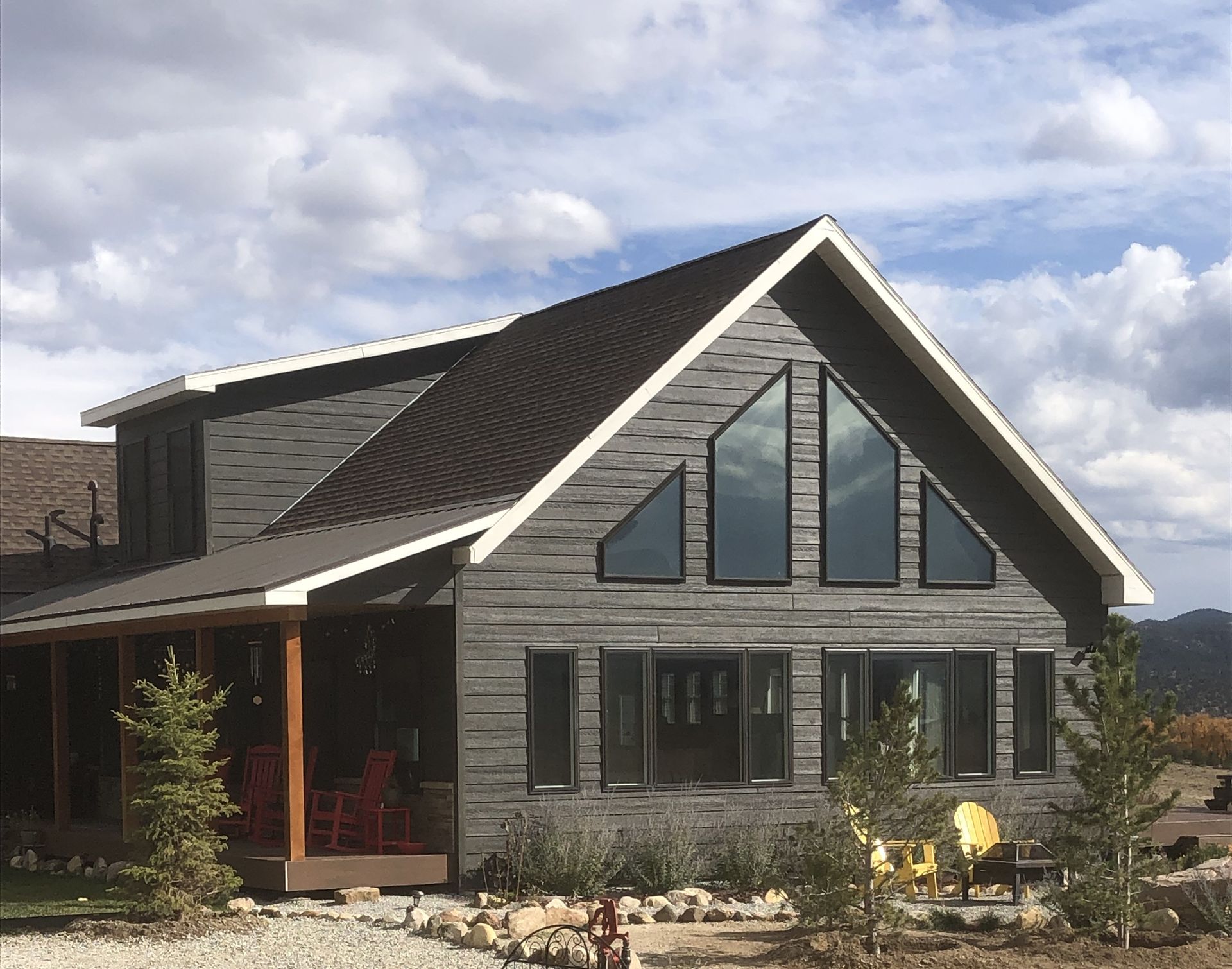 Modern gray house with steep gabled roof and large triangular windows under a cloudy sky
