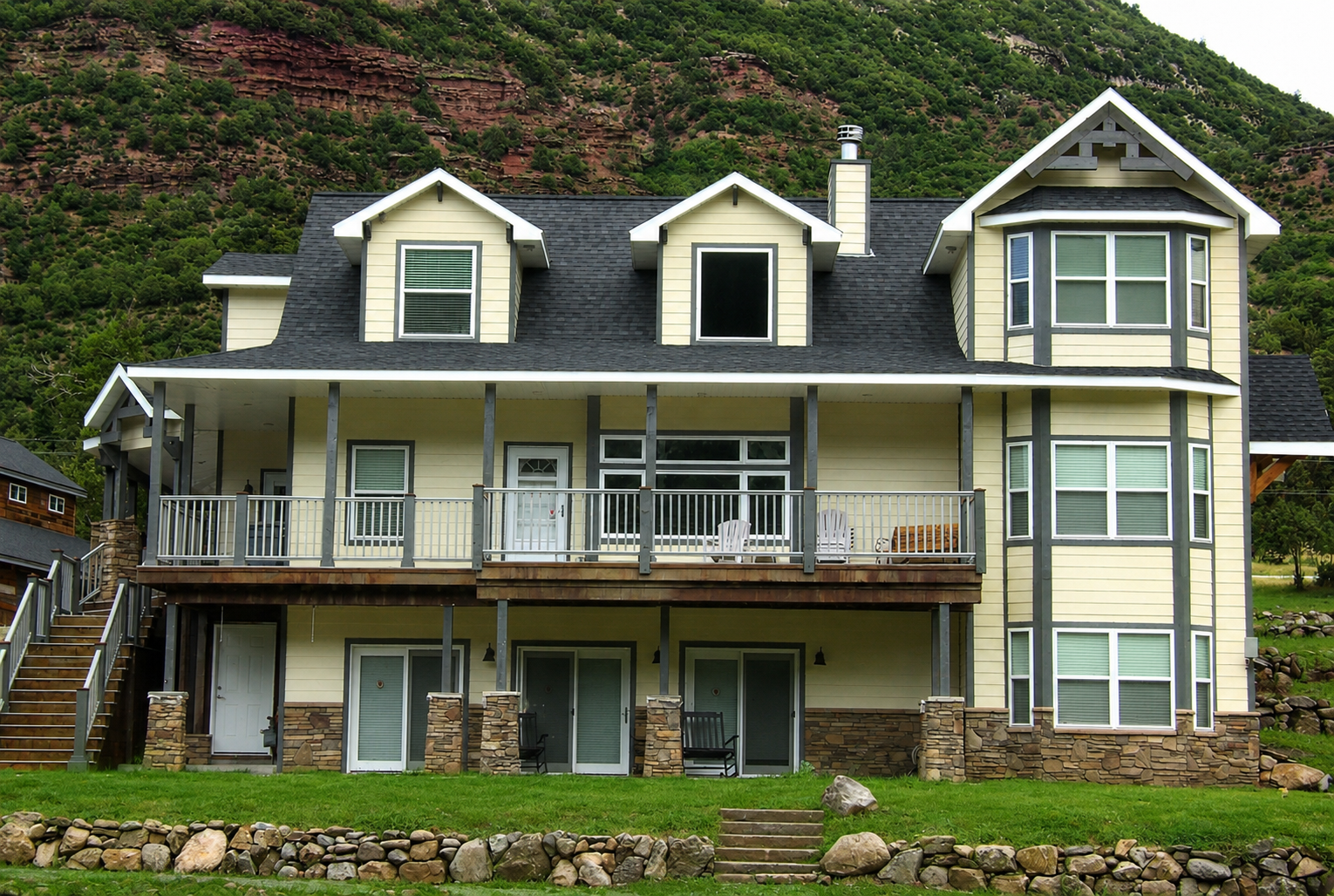 Two-story seaside house with gray roof, white trim, and green hillside backdrop