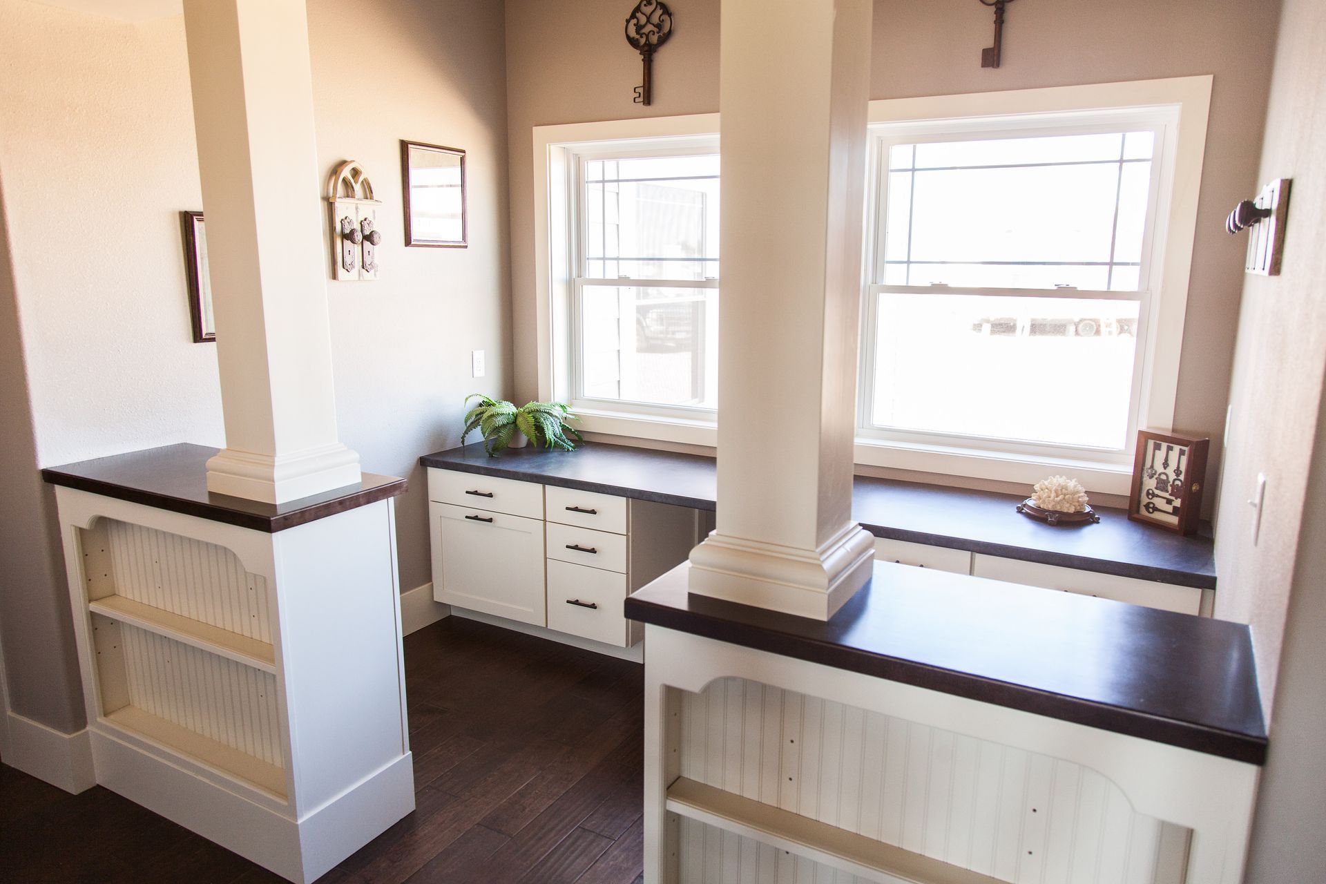 Sunlit window nook with built-in white cabinets, dark countertops, and a small plant on the center counter.