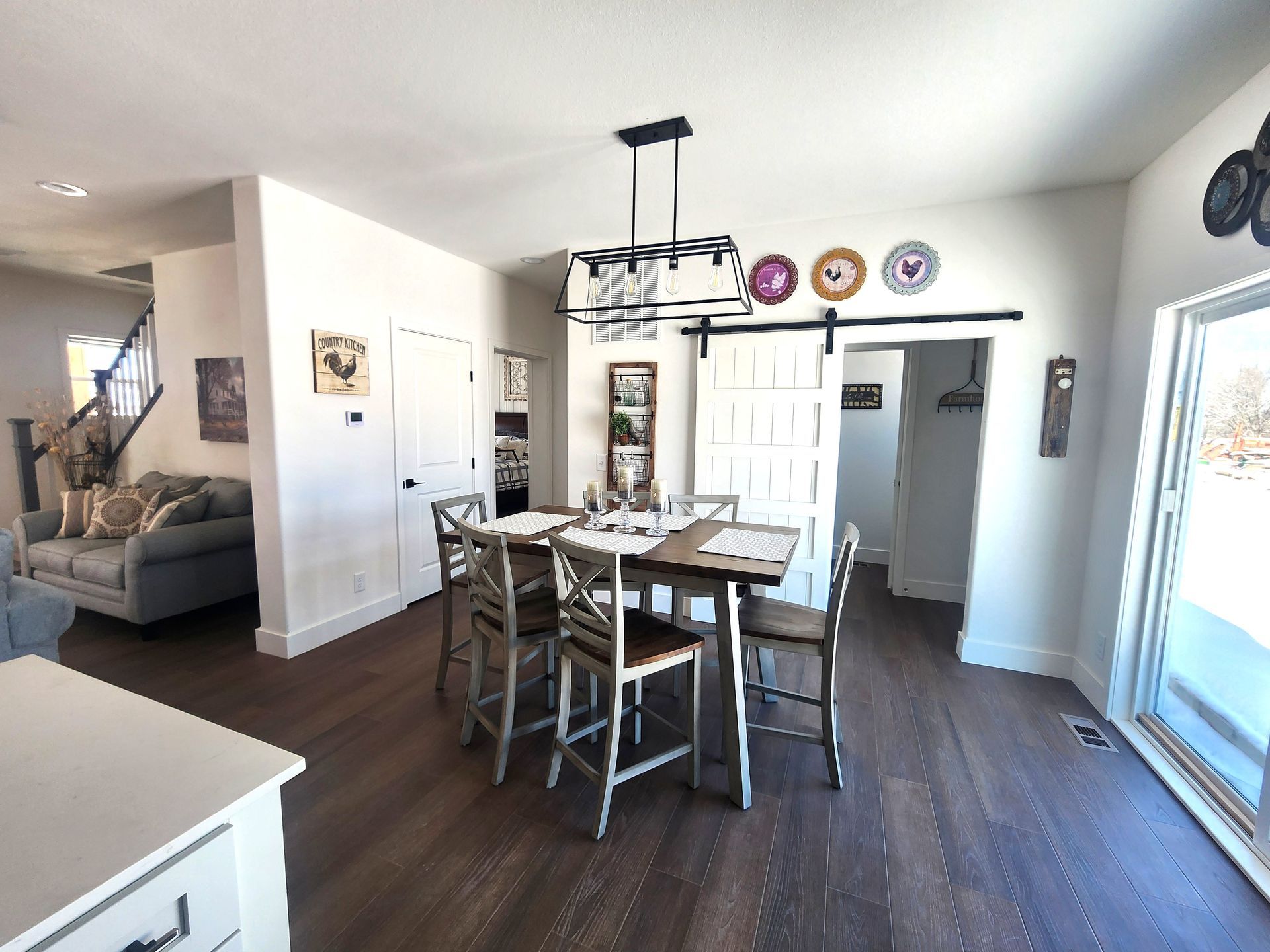 Bright dining room with wooden table, chairs, large windows, and open living area with gray sofa