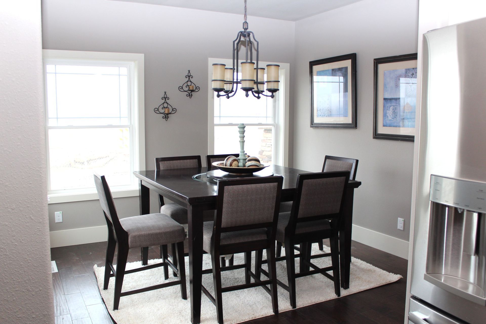 Dining room with dark wood table and chairs, chandelier, gray walls, and sunlight from the window.