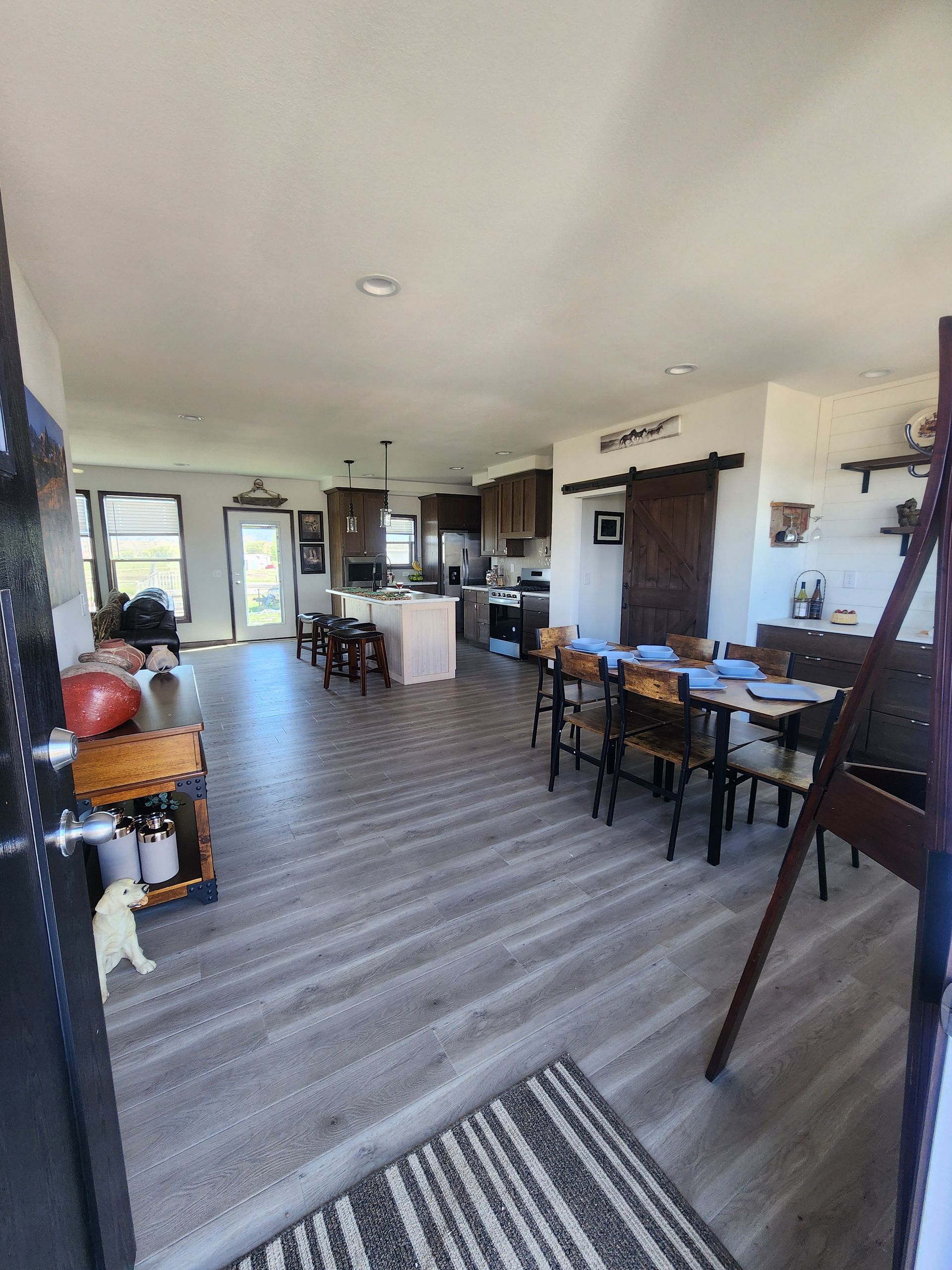 Long dining and living room with striped carpet, wooden table, chairs, piano, and large windows