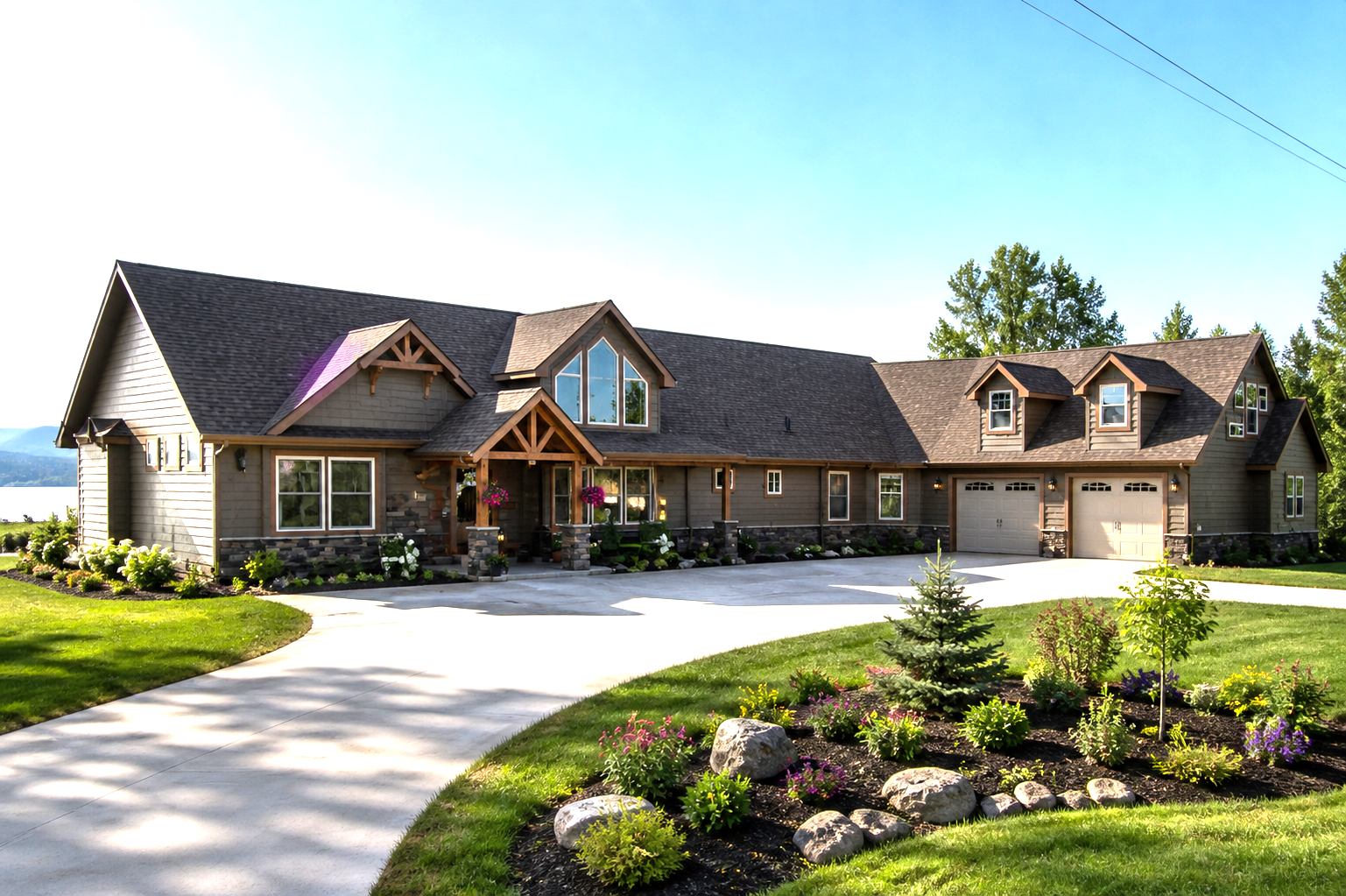 Large modern stone house with a curved driveway and landscaped front yard on a sunny day