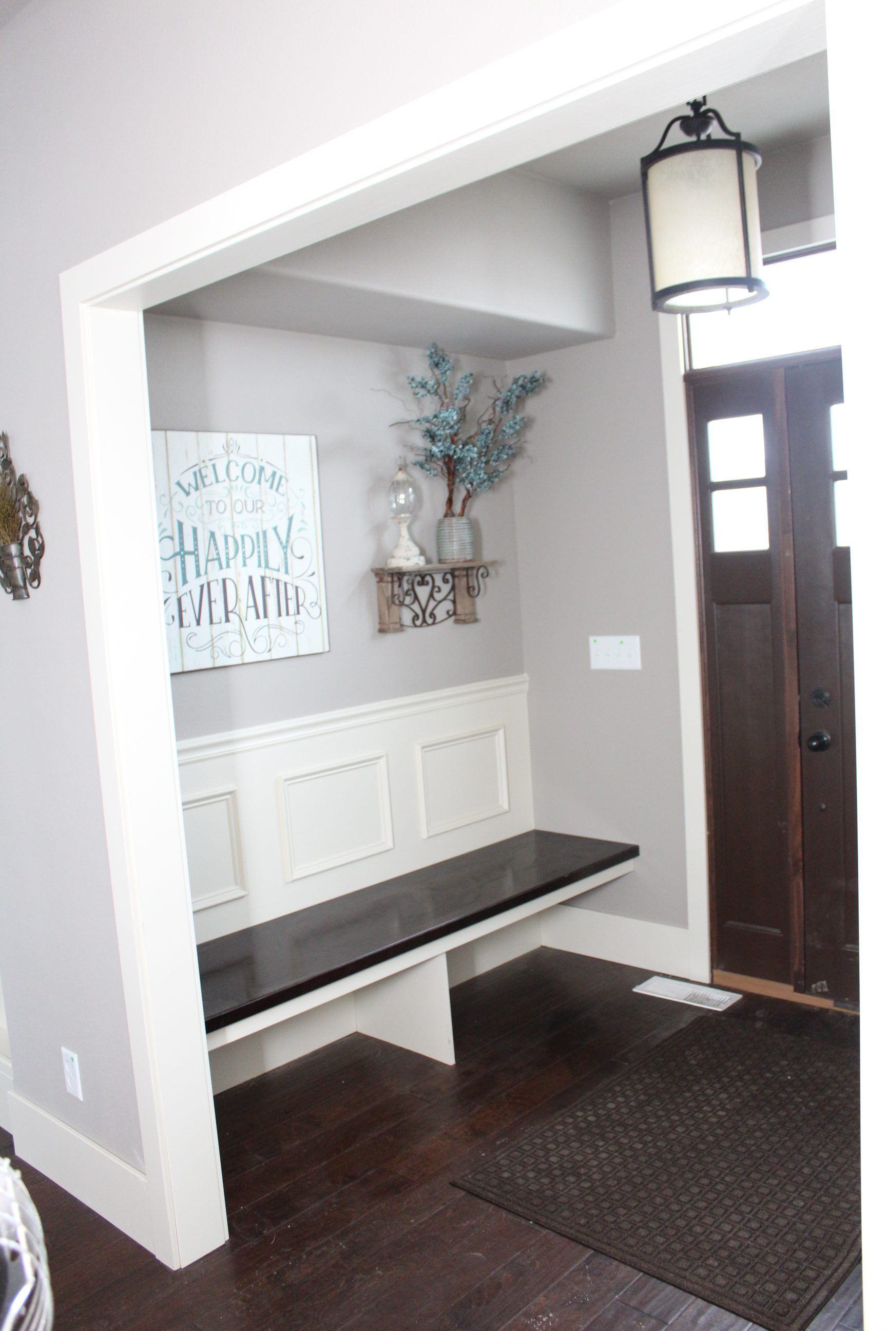 Entryway with bench, wall decor, hanging lantern, and dark front door on a brown rug