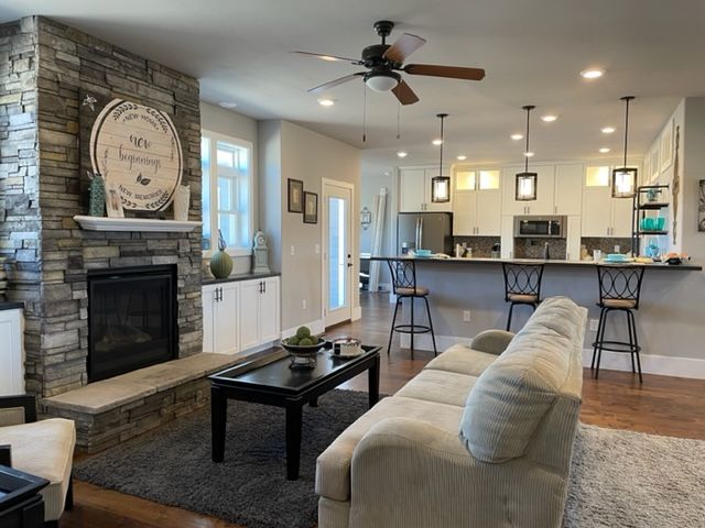 Bright open living room with stone fireplace, gray sofa, coffee table, and kitchen island with bar stools