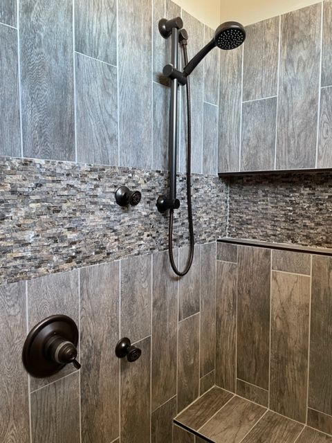 Bathroom shower with gray tile, mosaic accent strip, and black rainfall showerhead and fixtures