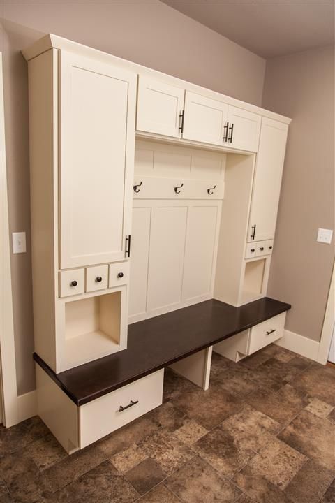White built-in hall tree with cabinets, hooks, bench, and cubbies against beige walls and tile floor.