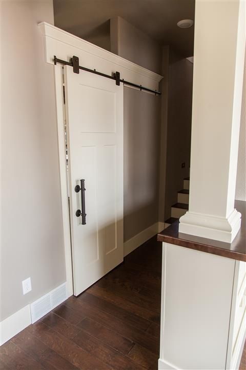 Interior hallway with a white sliding barn door, dark wood floor, and staircase in the background