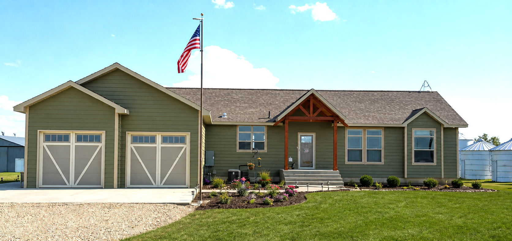 Single-story house with double garage, American flag, and landscaped front yard under a blue sky