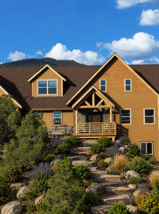 Wooden hillside house with stone steps, front porch, and blue sky with clouds