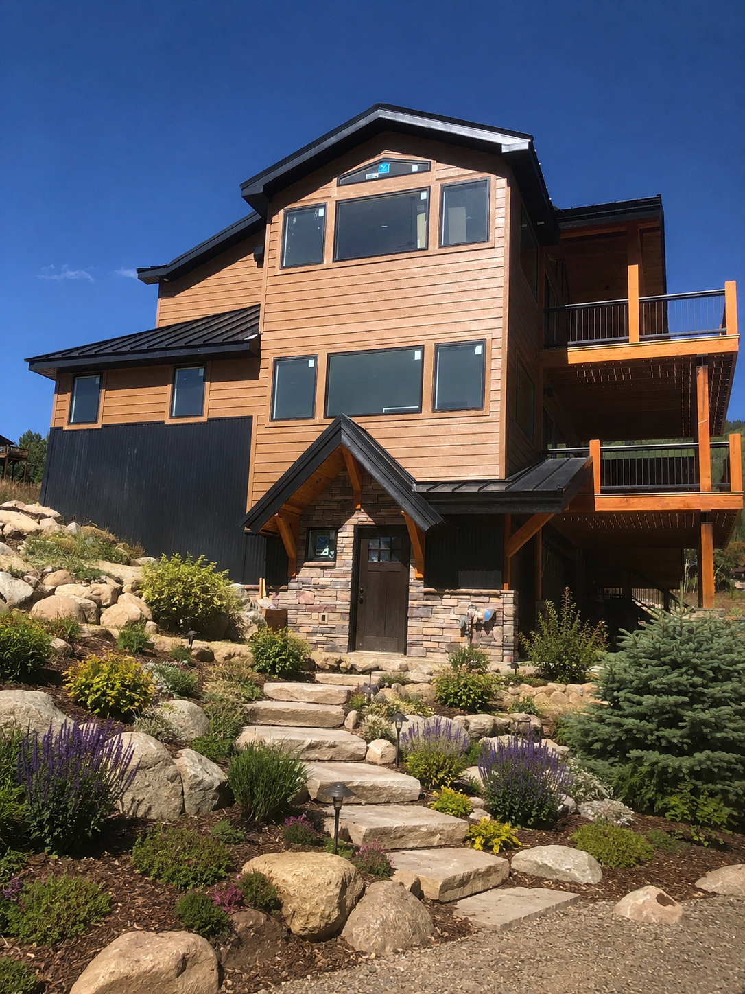 Modern multi-story house with stone path, landscaped garden, and blue sky