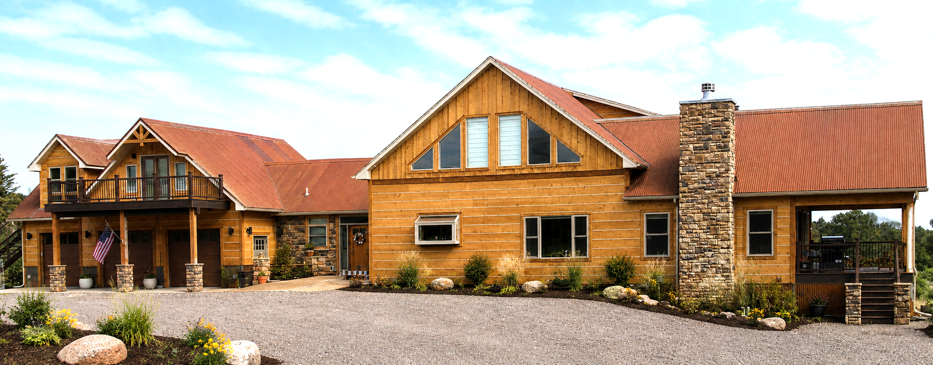 Rustic stone lodge with red roofs and a gravel driveway under a blue sky