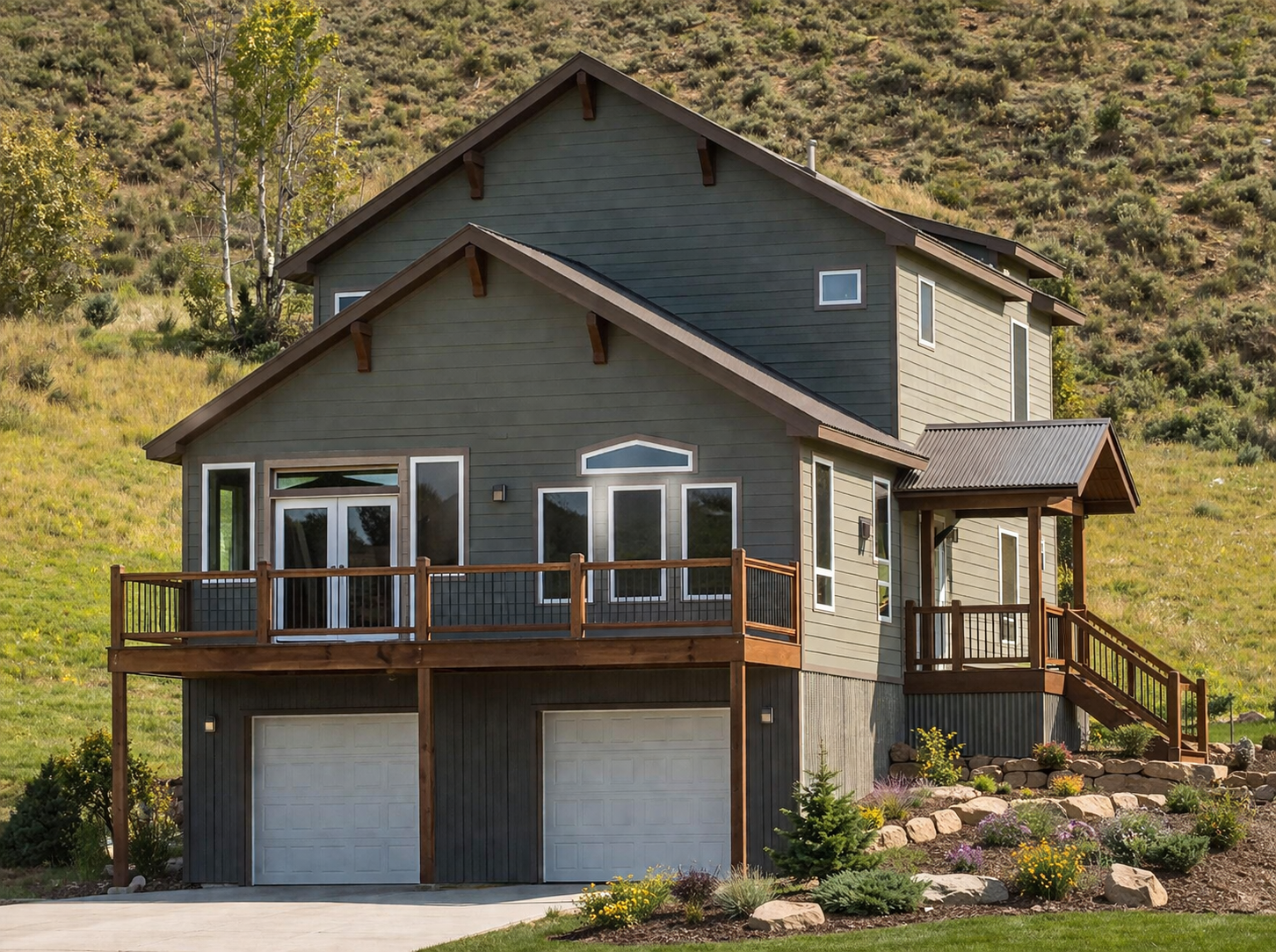 Two-story gray house with a wooden balcony, double garage, and hillside landscaping