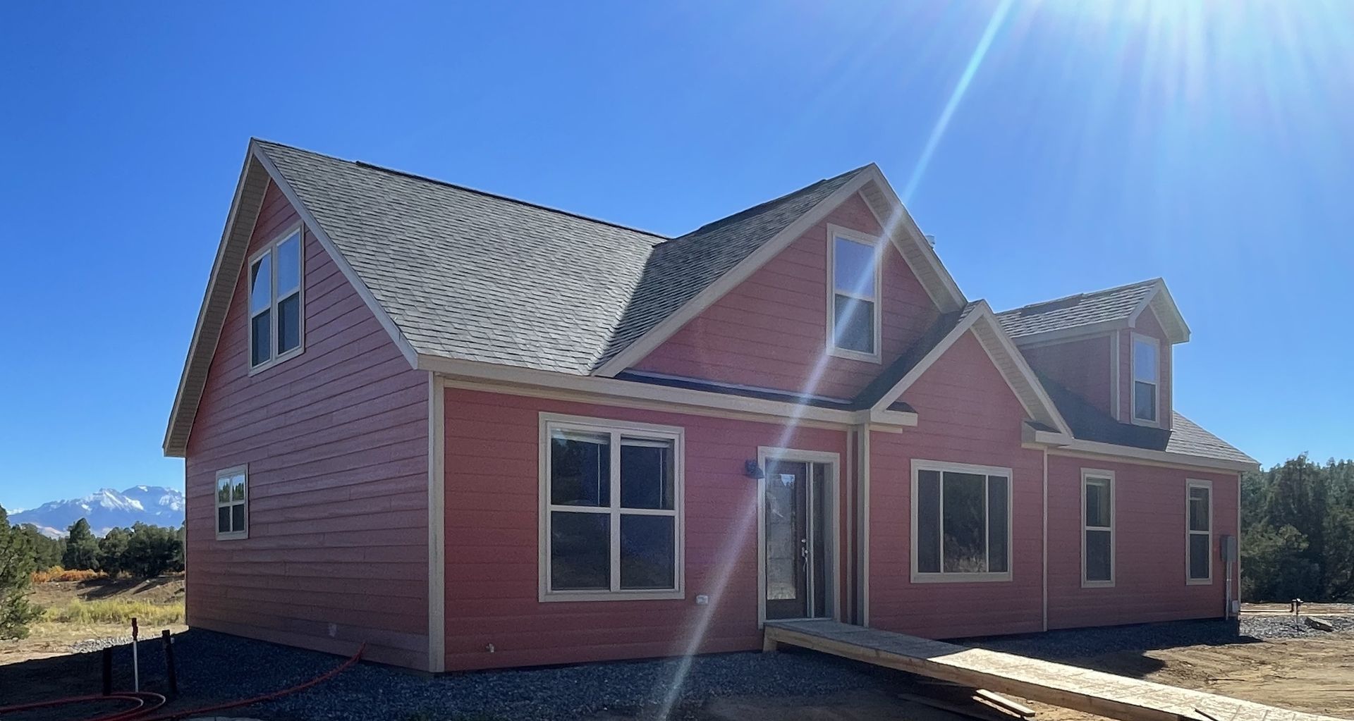 New pink house with gray roof under bright blue sky, viewed from the front-left angle