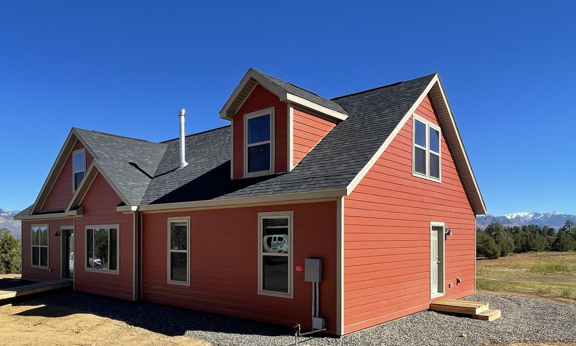 Red house with dark roof and white trim under a clear blue sky, set in a rural open area