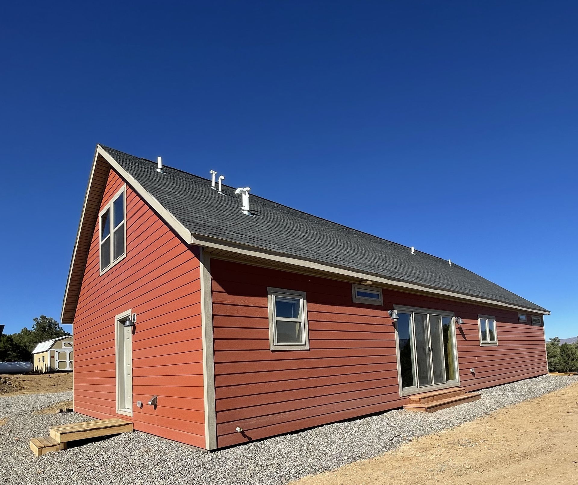 Red house with gray roof on a gravel lot under a clear blue sky