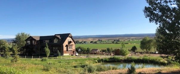 Stone house beside a green garden and pond, overlooking open countryside under a clear blue sky.