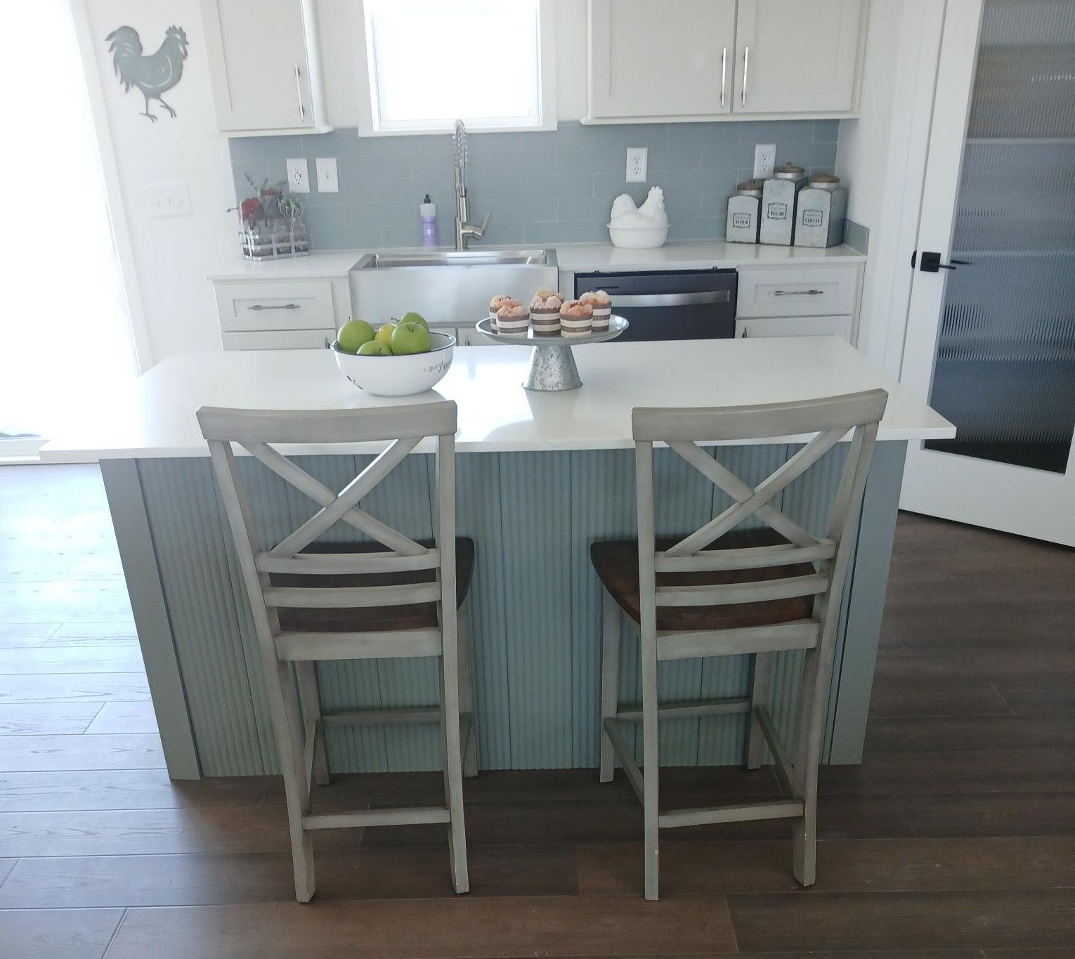 Bright white kitchen with island, two stools, fruit bowl, and rooster wall art