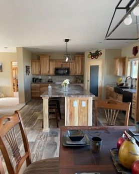 Open kitchen and dining area with wood cabinets, granite island, and dark dining table by large windows.