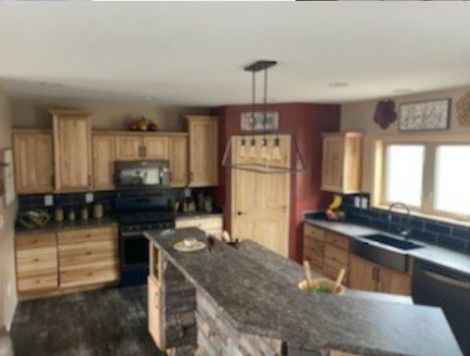 Spacious kitchen with wooden cabinets, granite island, black countertops, and windows over the sink.